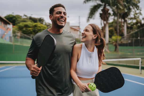 Couple playing pickleball celebrate point Apartment community resort-style pool with lounge chairs